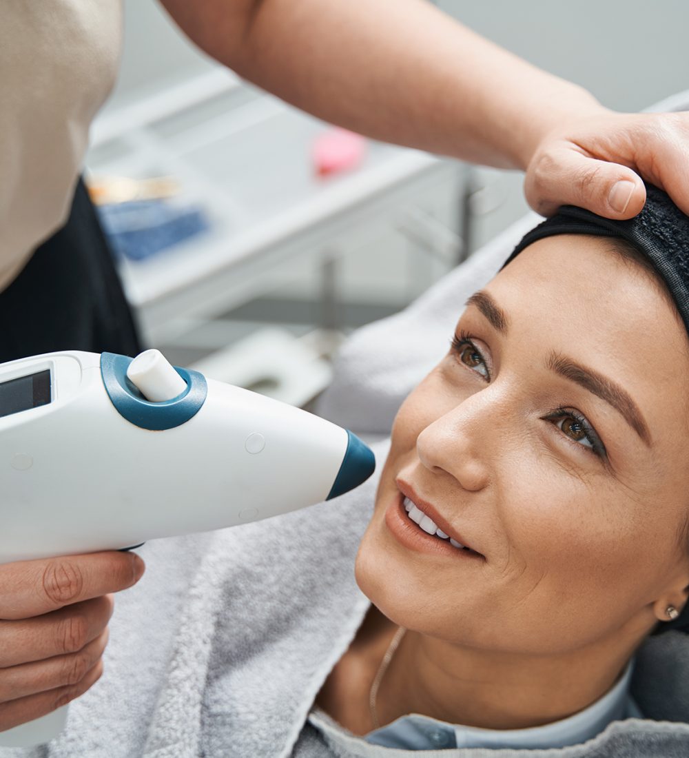 Professional dermatologist pointing a CO2 mesotherapy gun at the beautiful young Caucasian female patient face
